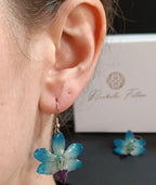 Ragazza indossa orecchini pendenti artigianali con piccole orchidee vere in resina trasparente, colore Azzurro con ganci in argento.