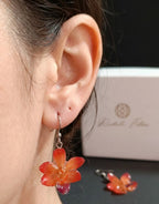 Ragazza indossa orecchini pendenti artigianali con piccole orchidee vere in resina trasparente, colore arancione con ganci in argento.