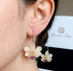 Ragazza indossa orecchini pendenti artigianali con piccole orchidee vere in resina trasparente, colore bianco con ganci in argento.