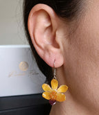 Ragazza indossa orecchini pendenti artigianali con piccole orchidee vere in resina trasparente, colore giallo con ganci in argento.