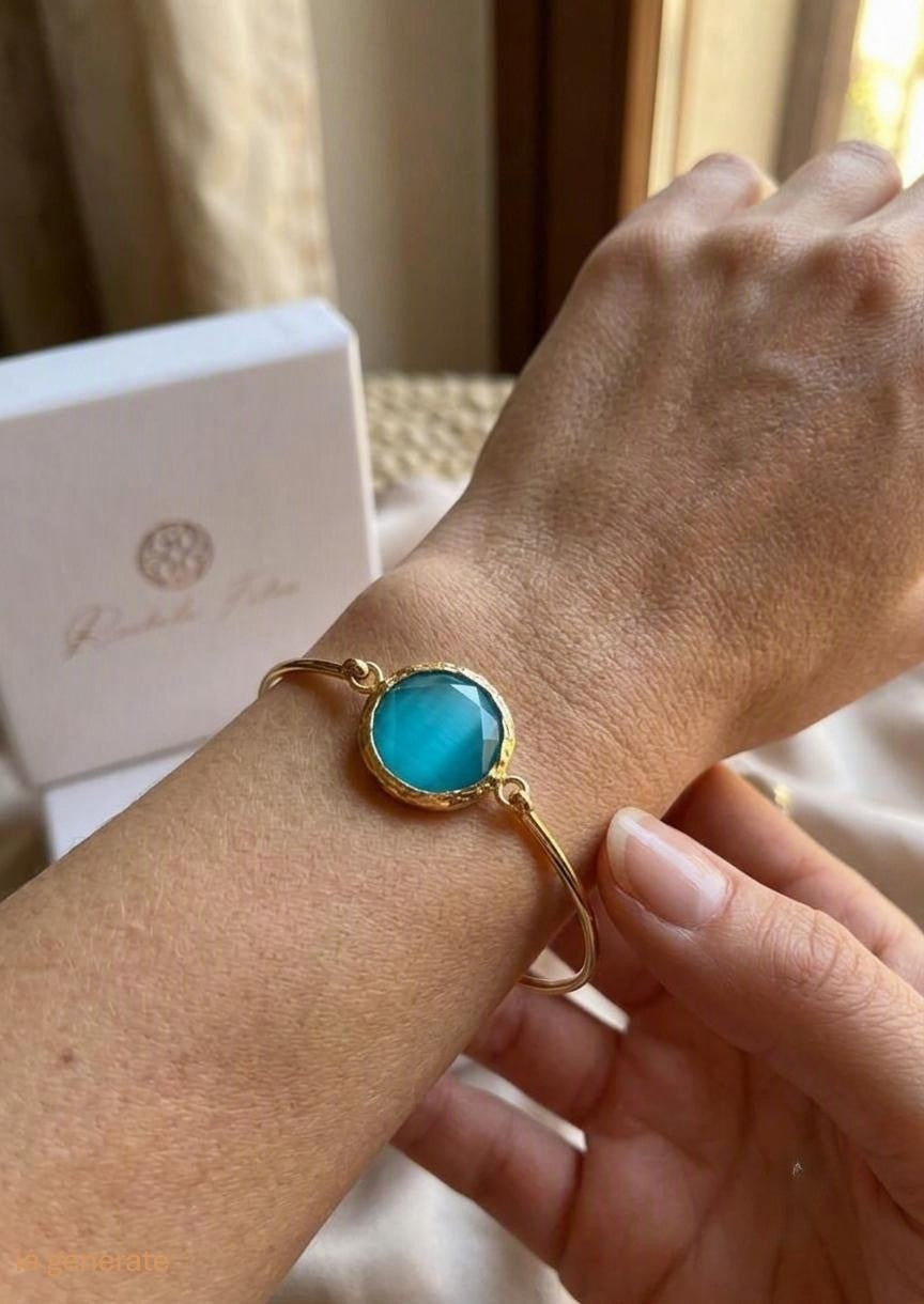 bracciale rigido in bronzo placcato oro opaco di Rachele Falvo con pietra centrale di occhio di gatto azzurro naturale sfaccettato.