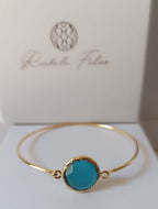 bracciale rigido in bronzo placcato oro opaco di Rachele Falvo con pietra centrale di occhio di gatto azzurro naturale sfaccettato.