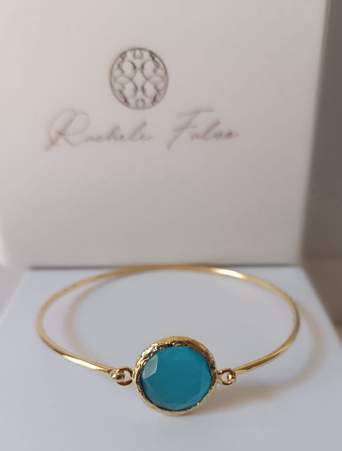 bracciale rigido in bronzo placcato oro opaco di Rachele Falvo con pietra centrale di occhio di gatto azzurro naturale sfaccettato.