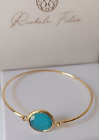 bracciale rigido in bronzo placcato oro opaco di Rachele Falvo con pietra centrale di occhio di gatto azzurro naturale sfaccettato.