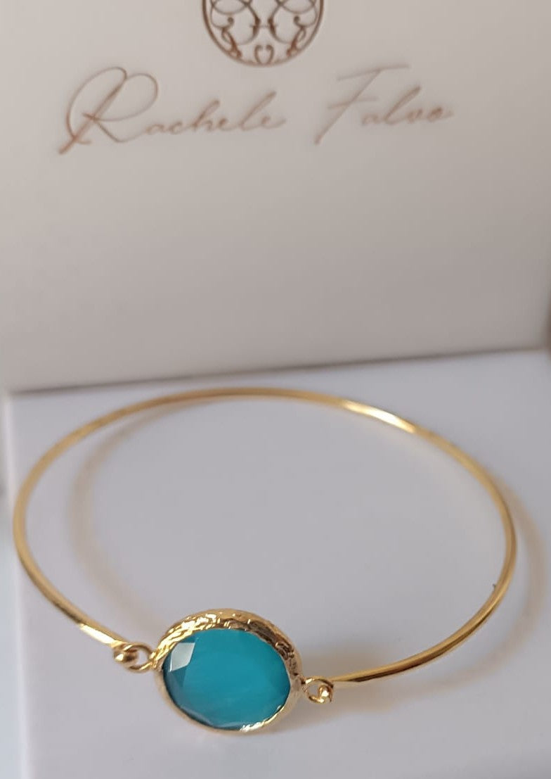 bracciale rigido in bronzo placcato oro opaco di Rachele Falvo con pietra centrale di occhio di gatto azzurro naturale sfaccettato.