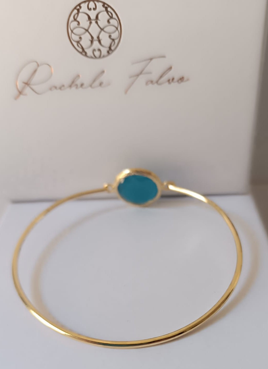 bracciale rigido in bronzo placcato oro opaco di Rachele Falvo con pietra centrale di occhio di gatto azzurro naturale sfaccettato.