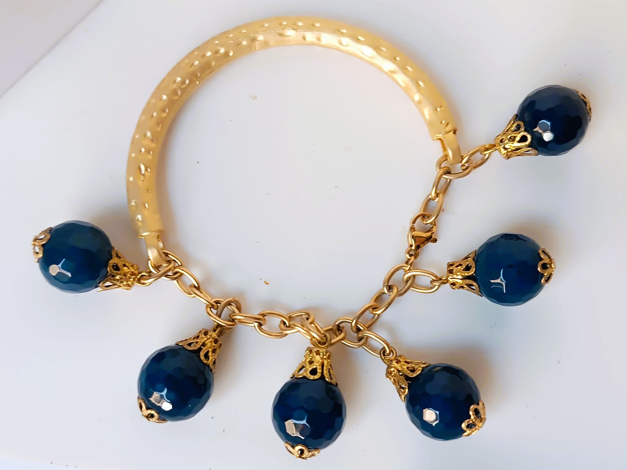 bracciale semirigido in bronzo placcato oro opaco di Rachele Falvo con fusto battuto e sei topazi azzurri naturali pendenti