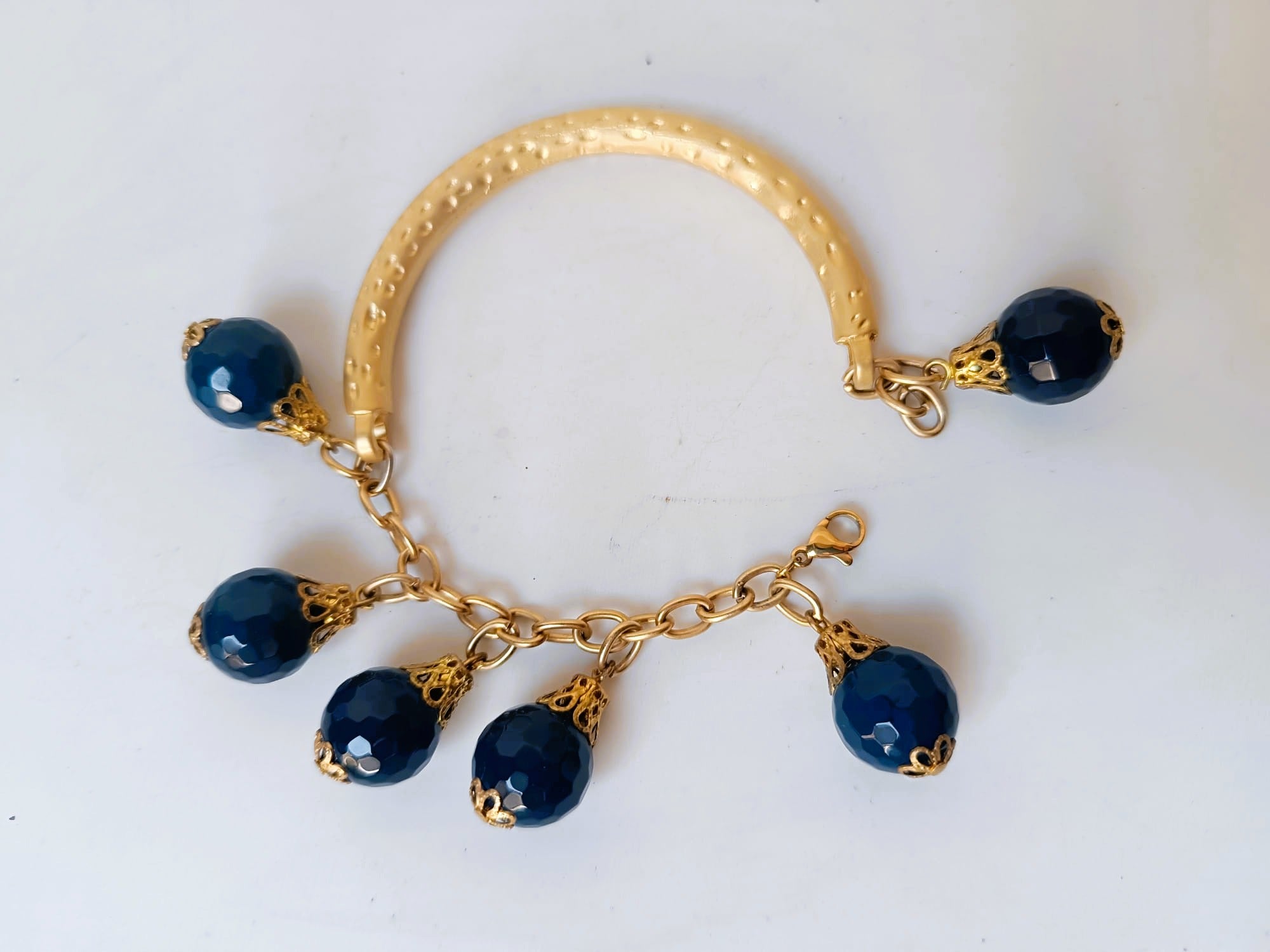 bracciale semirigido in bronzo placcato oro opaco di Rachele Falvo con fusto battuto e sei topazi azzurri naturali pendenti