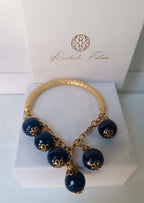 bracciale semirigido in bronzo placcato oro opaco di Rachele Falvo con fusto battuto e sei topazi azzurri naturali pendenti