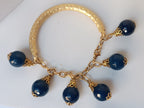bracciale semirigido in bronzo placcato oro opaco di Rachele Falvo con fusto battuto e sei topazi azzurri naturali pendenti