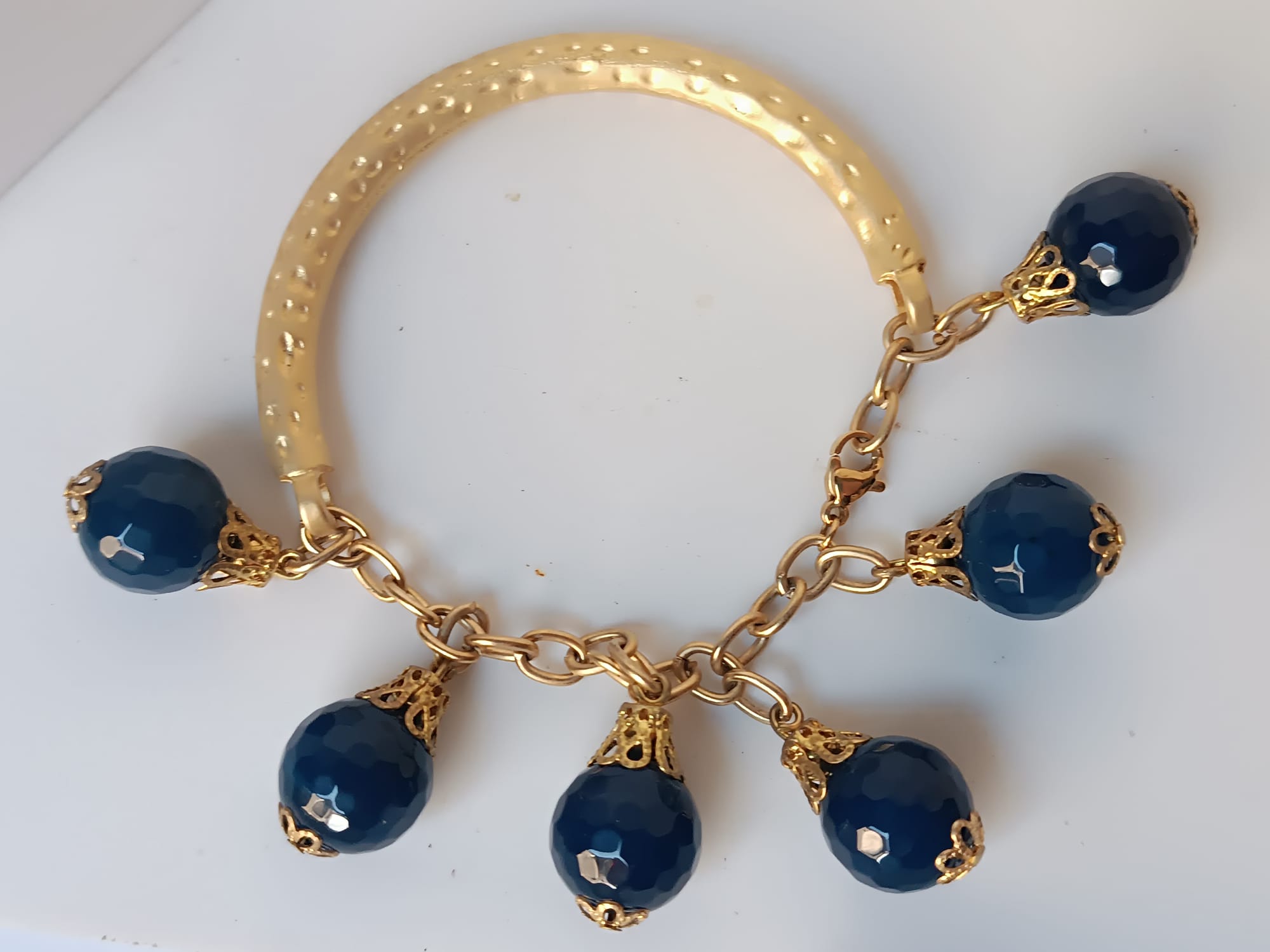 bracciale semirigido in bronzo placcato oro opaco di Rachele Falvo con fusto battuto e sei topazi azzurri naturali pendenti