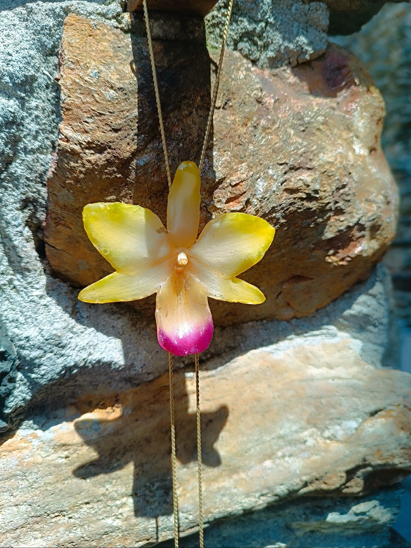 Collana artigianale con un ciondolo realizzato con una vera orchidea gialla sfumata in rosa sul labello, inglobata in resina trasparente e lucida. Il ciondolo è appeso a una catenina ritorta dorata in oro su bronzo