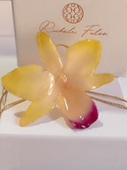 Collana artigianale con un ciondolo realizzato con una vera orchidea gialla sfumata in rosa sul labello, inglobata in resina trasparente e lucida. Il ciondolo è appeso a una catenina ritorta dorata in oro su bronzo