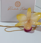 Collana artigianale con un ciondolo realizzato con una vera orchidea gialla sfumata in rosa sul labello, inglobata in resina trasparente e lucida. Il ciondolo è appeso a una catenina ritorta dorata in oro su bronzo