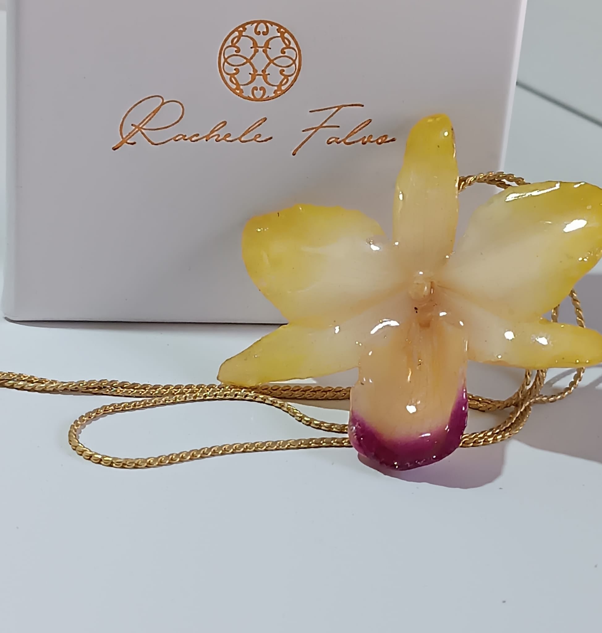 Collana artigianale con un ciondolo realizzato con una vera orchidea gialla sfumata in rosa sul labello, inglobata in resina trasparente e lucida. Il ciondolo è appeso a una catenina ritorta dorata in oro su bronzo