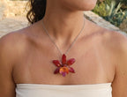 Ciondolo artigianale con vera orchidea marrone e arancio racchiusa in resina trasparente con riflessi di luce, mostrato con catenina in acciaio color oro e color argento.