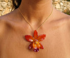 Ciondolo artigianale con vera orchidea marrone e arancio racchiusa in resina trasparente con riflessi di luce, mostrato con catenina in acciaio color oro e color argento.