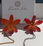 Ciondolo artigianale con vera orchidea marrone e arancio racchiusa in resina trasparente con riflessi di luce, mostrato con catenina in acciaio color oro e color argento.