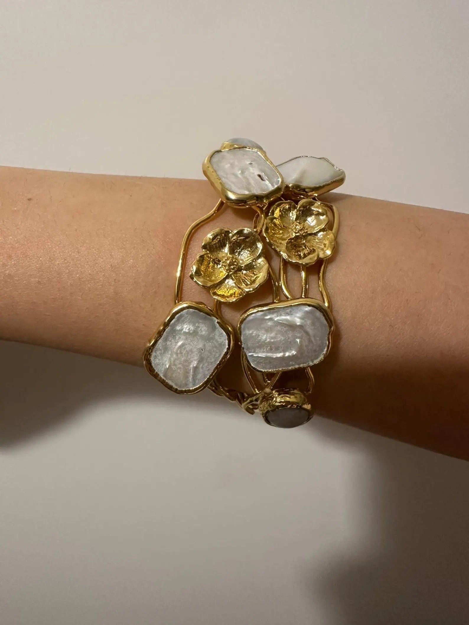 Bracciale rigido multifilo regolabile firmato Rachele Falvo in bronzo dorato, decorato con fiori scultorei in rilievo e grandi placche geometriche di madreperla naturale lucida