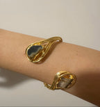Bracciale scultoreo rigido a spira contrarié firmato Rachele Falvo, realizzato in fili di bronzo dorato intrecciati a mano con incastonate un'agata striata naturale e un'ametista in druza grezza,