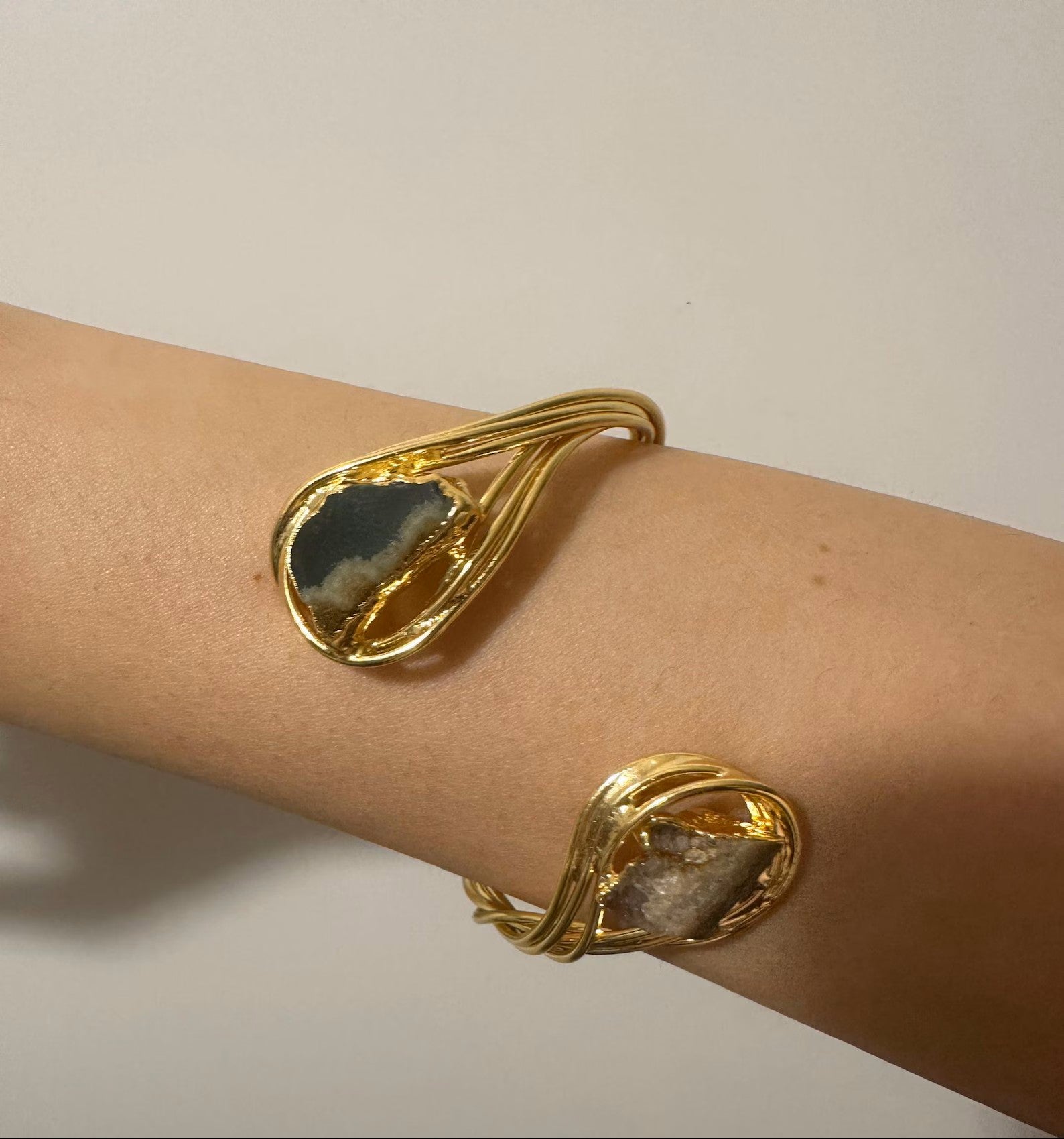 Bracciale scultoreo rigido a spira contrarié firmato Rachele Falvo, realizzato in fili di bronzo dorato intrecciati a mano con incastonate un'agata striata naturale e un'ametista in druza grezza,