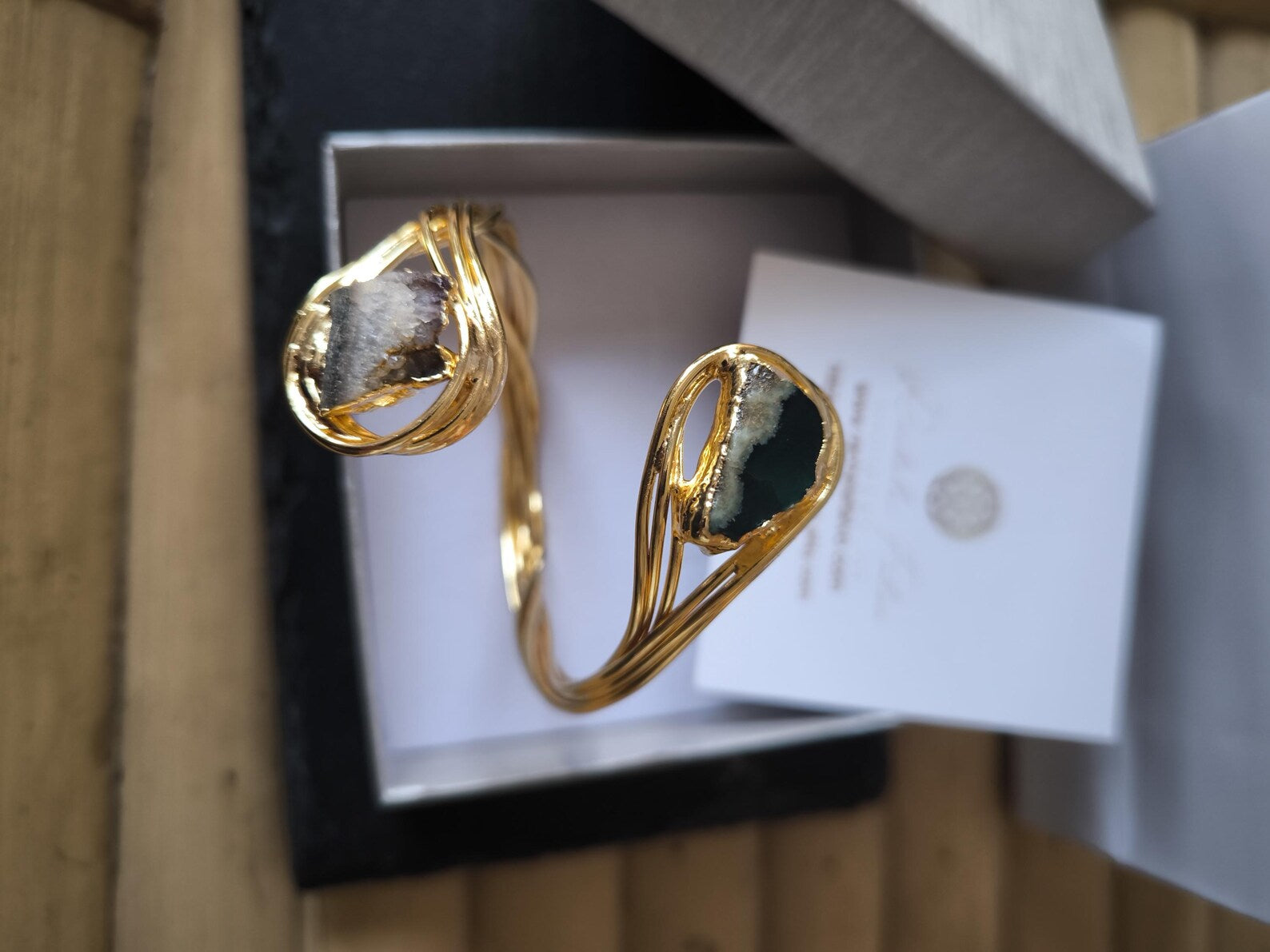 Bracciale scultoreo rigido a spira contrarié firmato Rachele Falvo, realizzato in fili di bronzo dorato intrecciati a mano con incastonate un'agata striata naturale e un'ametista in druza grezza,