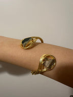 Bracciale scultoreo rigido a spira contrarié firmato Rachele Falvo, realizzato in fili di bronzo dorato intrecciati a mano con incastonate un'agata striata naturale e un'ametista in druza grezza,