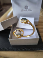 Bracciale scultoreo rigido a spira contrarié firmato Rachele Falvo, realizzato in fili di bronzo dorato intrecciati a mano con incastonate un'agata striata naturale e un'ametista in druza grezza,