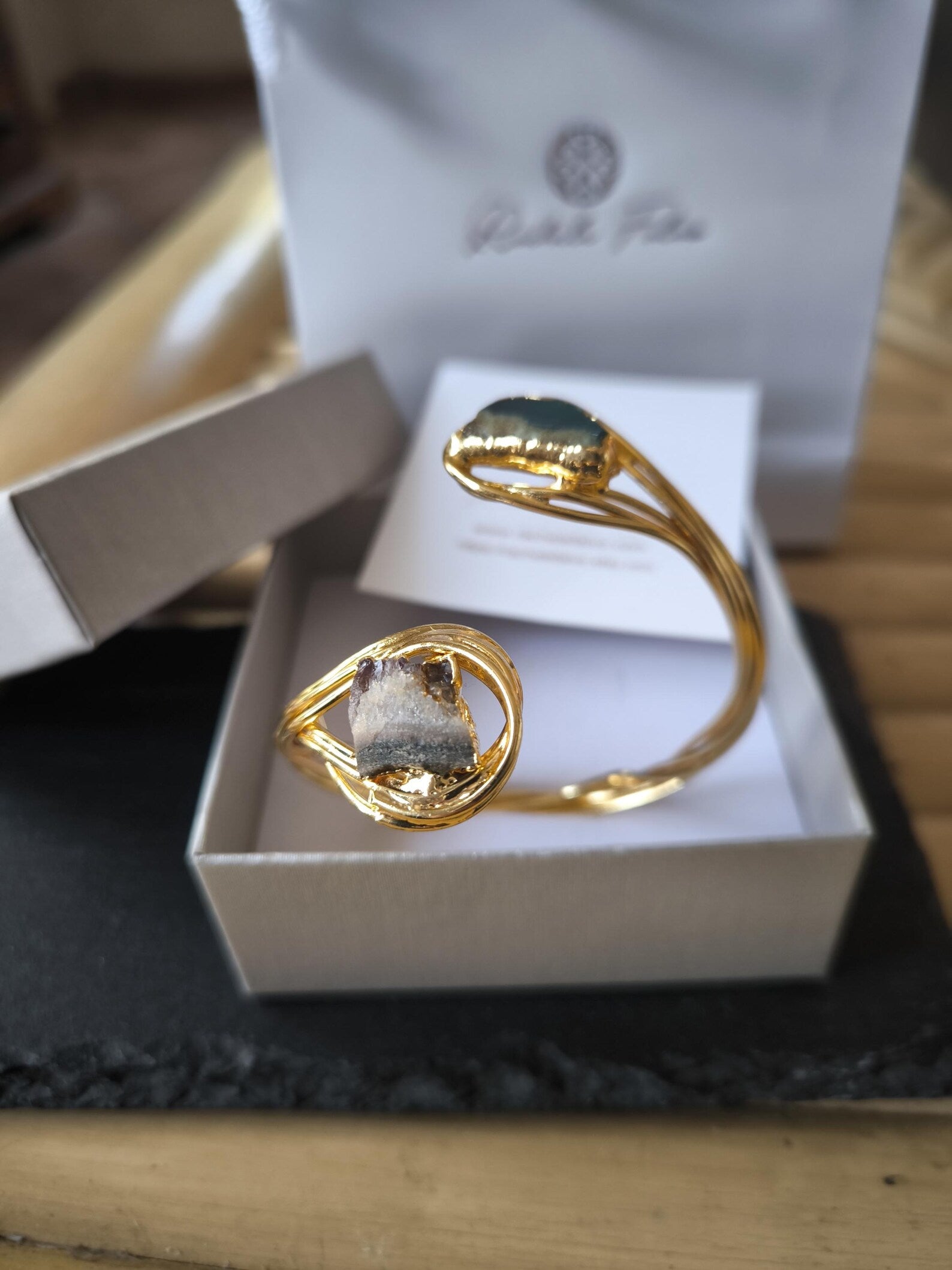Bracciale scultoreo rigido a spira contrarié firmato Rachele Falvo, realizzato in fili di bronzo dorato intrecciati a mano con incastonate un'agata striata naturale e un'ametista in druza grezza,