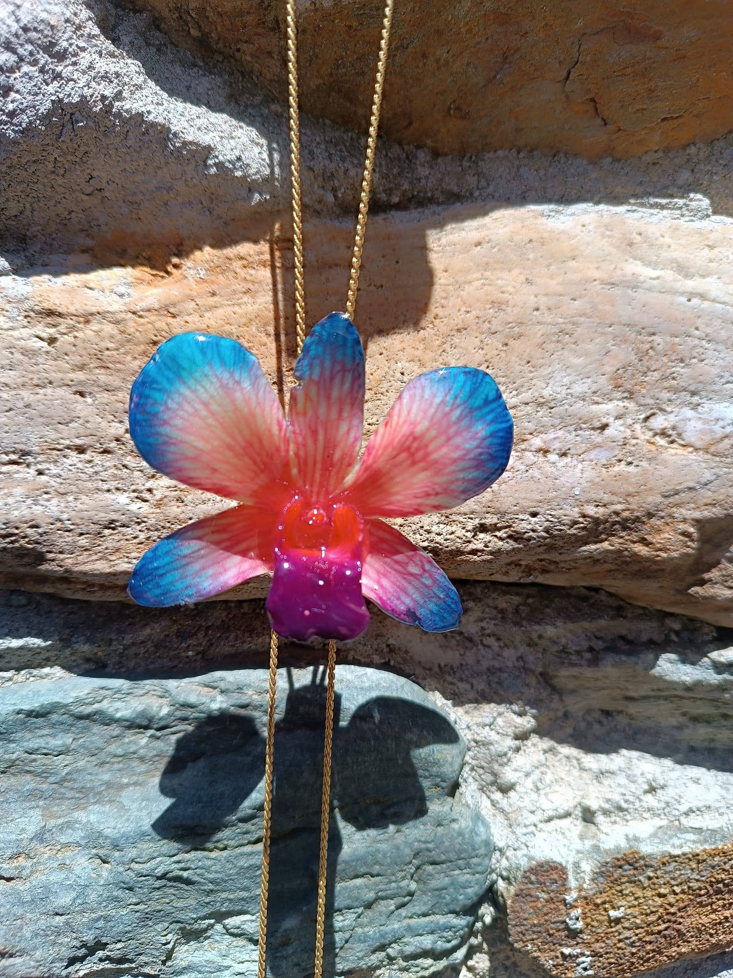 Collana con orchidea naturale azzurra e rossa inglobata in resina e saliscendi oro su bronzo regolabile