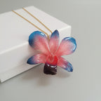 Collana con orchidea naturale azzurra e rossa inglobata in resina e saliscendi oro su bronzo regolabile