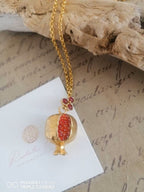 Collana dorata artigianale con ciondolo a melagrana in oro su bronzo e granatini rossi, simbolo di prosperità e abbondanza, dal design elegante e moderno