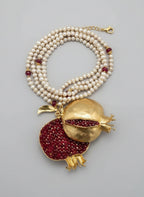 Collana artigianale ispirata al melograno con ciondolo in bronzo e granatini rossi, filo di perle bianche e dettagli borgogna e oro, design artistico e simbolico.