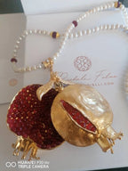 Collana artigianale ispirata al melograno con ciondolo in bronzo e granatini rossi, filo di perle bianche e dettagli borgogna e oro, design artistico e simbolico.