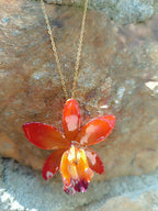 Ciondolo artigianale con vera orchidea marrone e arancio racchiusa in resina trasparente con riflessi di luce, mostrato con catenina in acciaio color oro e color argento.