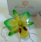 Ciondolo artigianale con vera orchidea gialla e verde racchiusa in resina trasparente che cattura la luce mostrando sfumature diverse, con catena saliscendi in argento su bronzo.