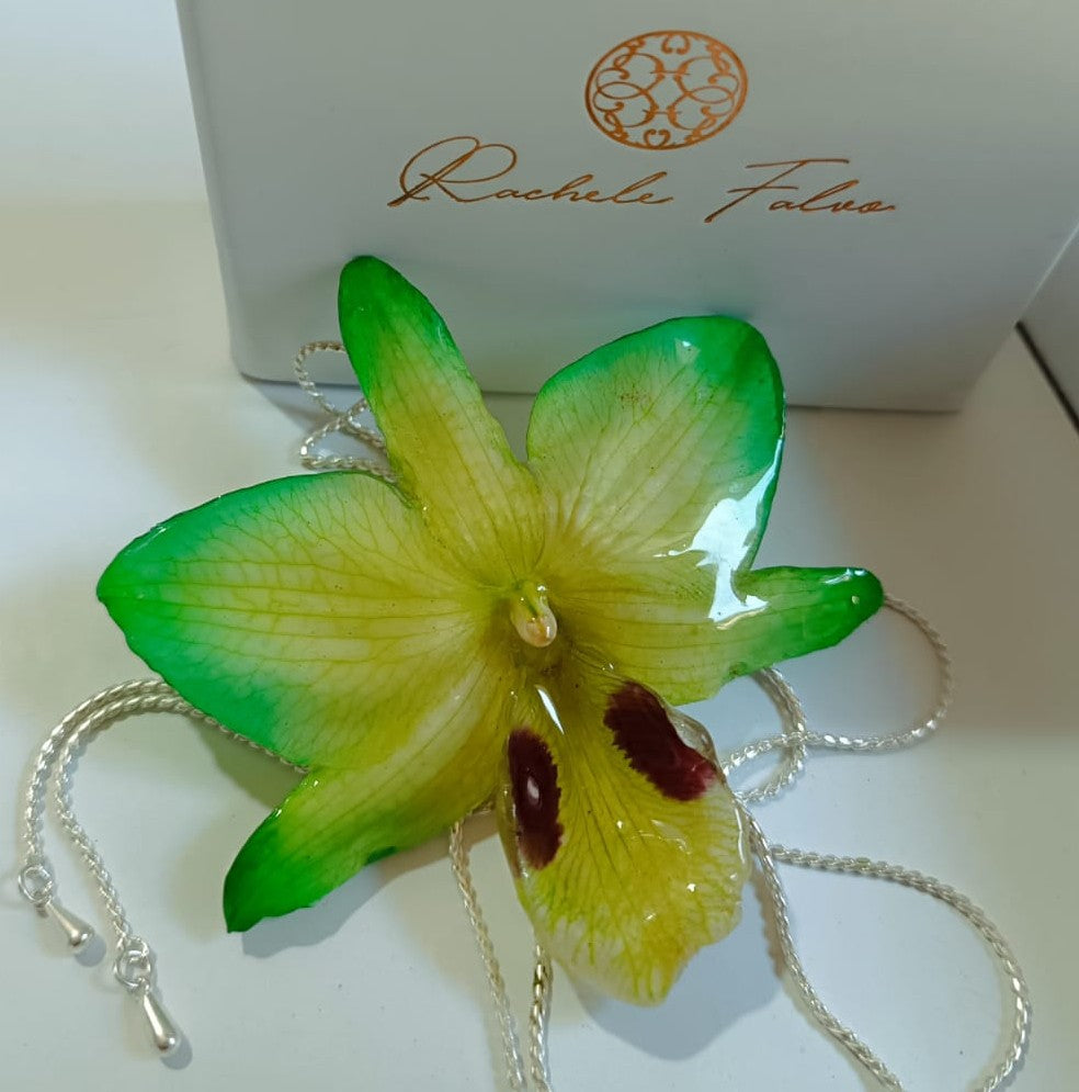 Ciondolo artigianale con vera orchidea gialla e verde racchiusa in resina trasparente che cattura la luce mostrando sfumature diverse, con catena saliscendi in argento su bronzo.