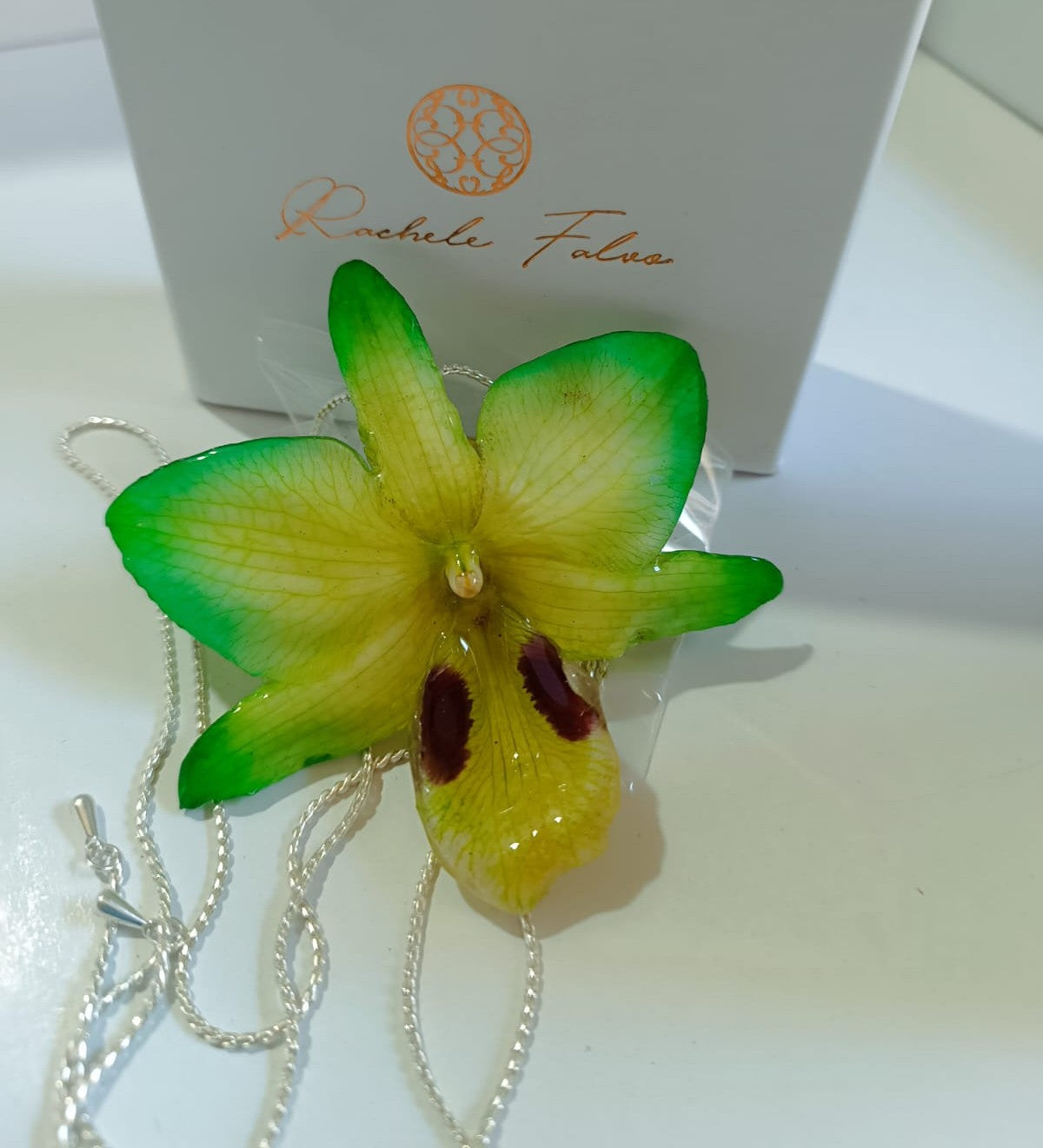 Ciondolo artigianale con vera orchidea gialla e verde racchiusa in resina trasparente che cattura la luce mostrando sfumature diverse, con catena saliscendi in argento su bronzo.