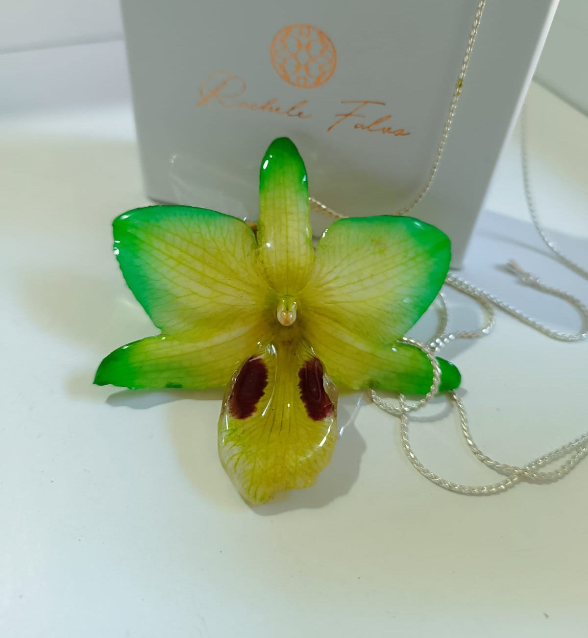 Ciondolo artigianale con vera orchidea gialla e verde racchiusa in resina trasparente che cattura la luce mostrando sfumature diverse, con catena saliscendi in argento su bronzo.