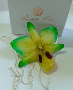 Ciondolo artigianale con vera orchidea gialla e verde racchiusa in resina trasparente che cattura la luce mostrando sfumature diverse, con catena saliscendi in argento su bronzo.