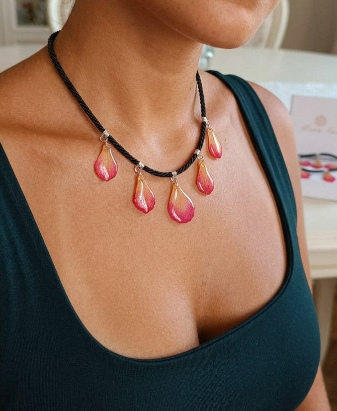 Primo piano di una collana artigianale in seta intrecciata color charcoal con cinque pendenti a goccia in resina trasparente contenenti petali di vera orchidea rosa e crema