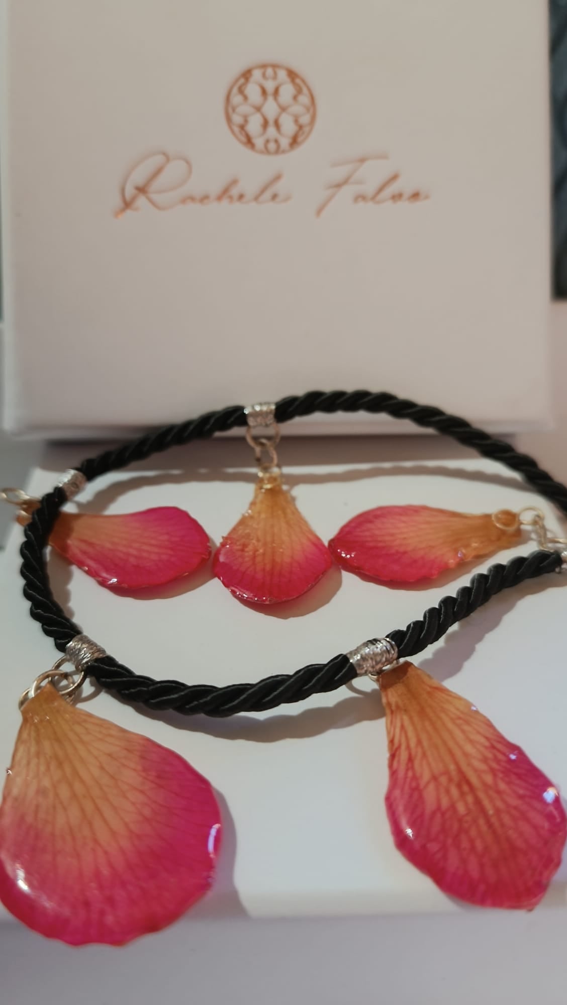 Primo piano di una collana artigianale in seta intrecciata color charcoal con cinque pendenti a goccia in resina trasparente contenenti petali di vera orchidea rosa e crema