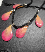 Primo piano di una collana artigianale in seta intrecciata color charcoal con cinque pendenti a goccia in resina trasparente contenenti petali di vera orchidea rosa e crema
