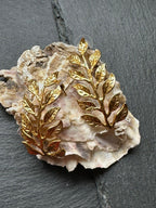 Orecchini dorati artigianali in oro su bronzo a forma di ramo fogliato con dettagli scolpiti, design elegante ispirato alla natura.