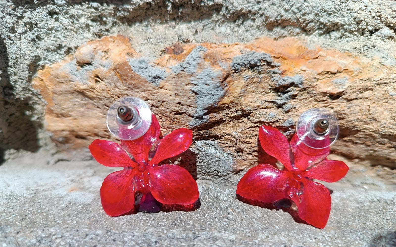 Coppia di piccoli orecchini artigianali al lobo a forma di orchidea vera di colore rosso intenso con sfumature viola al centro, inglobati in resina lucida