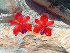 Coppia di piccoli orecchini artigianali al lobo a forma di orchidea vera di colore rosso intenso con sfumature viola al centro, inglobati in resina lucida