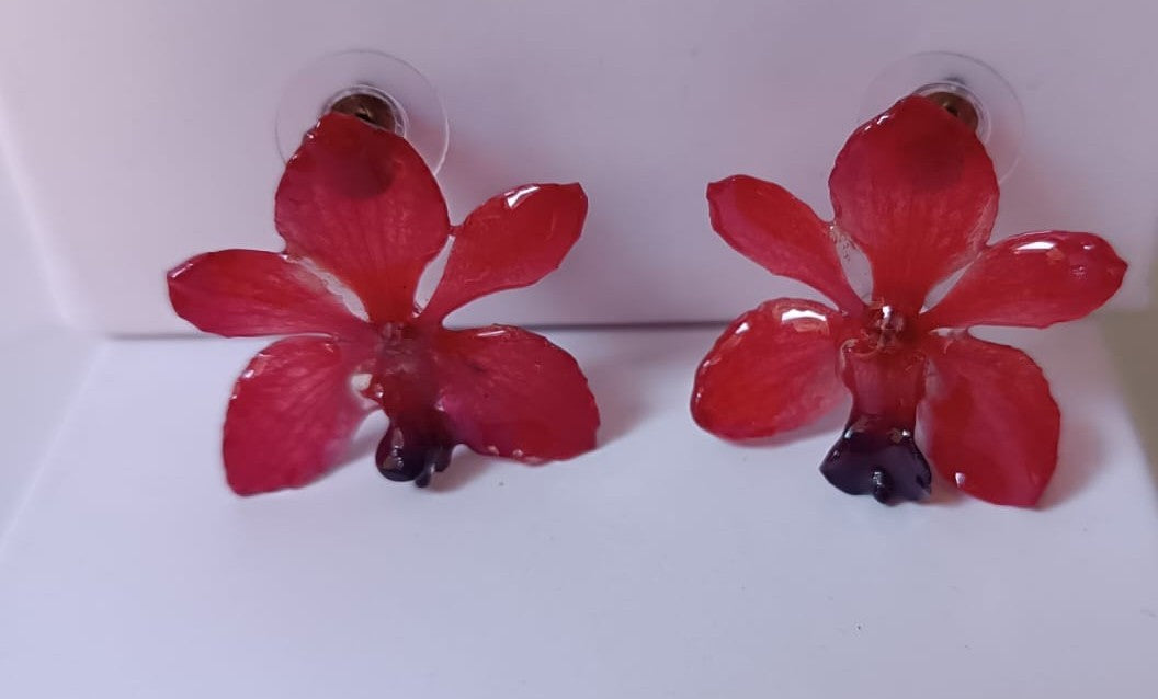 Coppia di piccoli orecchini artigianali al lobo a forma di orchidea vera di colore rosso intenso con sfumature viola al centro, inglobati in resina lucida