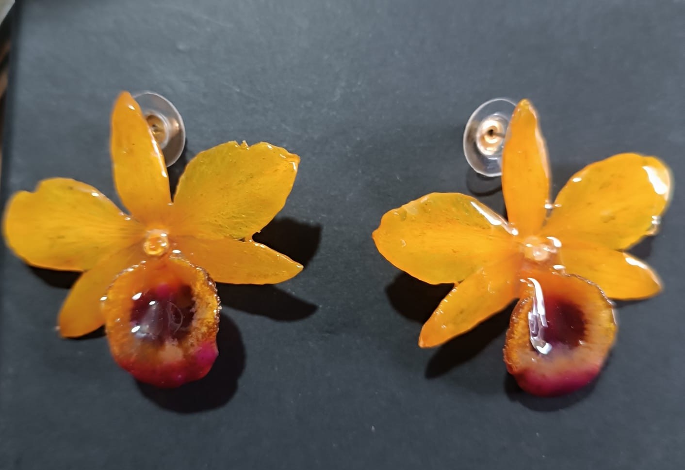 orecchini artigianali al lobo realizzati con intere orchidee vere in resina lucida, una variante  giallo ocra con sfumature viola, disposte sulla loro scatola regalo bianca firmata Rachele Falvo.