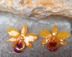 orecchini artigianali al lobo realizzati con intere orchidee vere in resina lucida, una variante  giallo ocra con sfumature viola, disposte sulla loro scatola regalo bianca firmata Rachele Falvo.