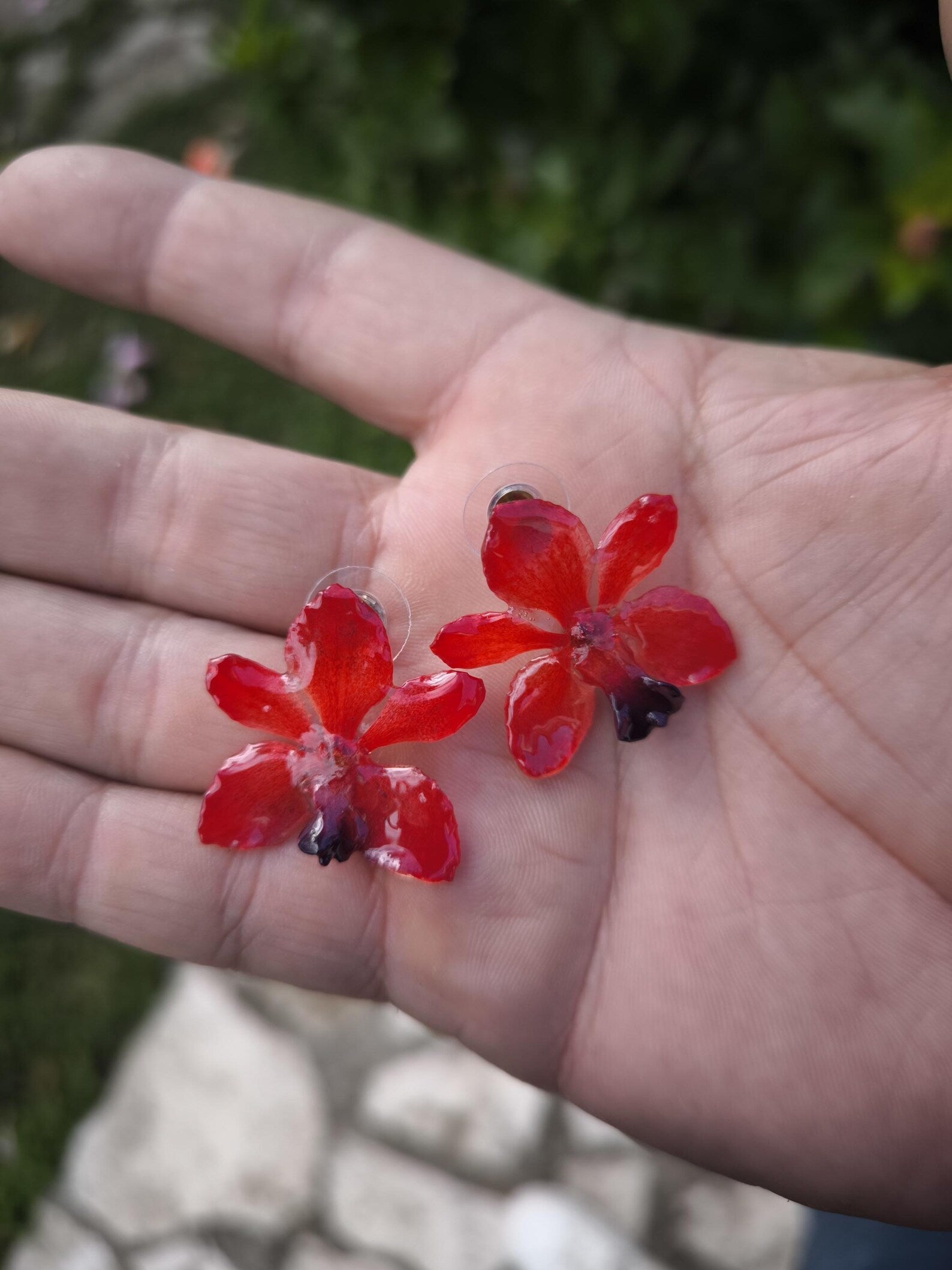 Coppia di piccoli orecchini artigianali al lobo a forma di orchidea vera di colore rosso intenso con sfumature viola al centro, inglobati in resina lucida